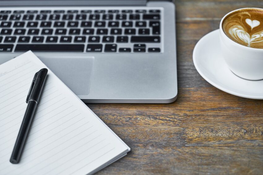laptop met notitieboekje en cappuccino